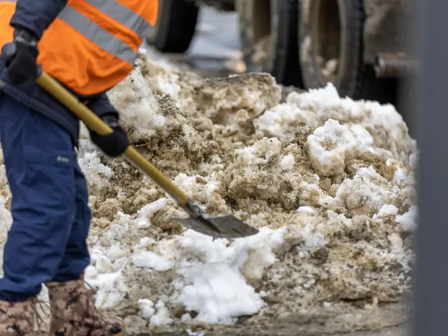 Mitarbeiter in Warnweste räumt mit der Schneeschaufel Schnee und Eis